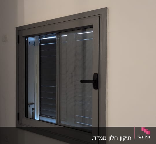 חלון עם תריסים אפורים מותקנים על קיר לבן